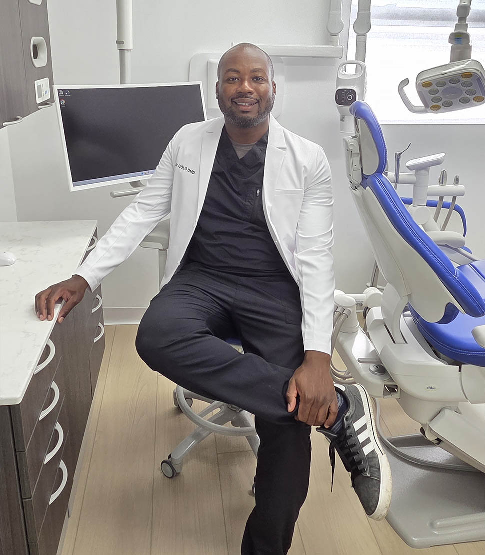 A man wearing a white lab coat sitting on a chair in front of dental equipment.