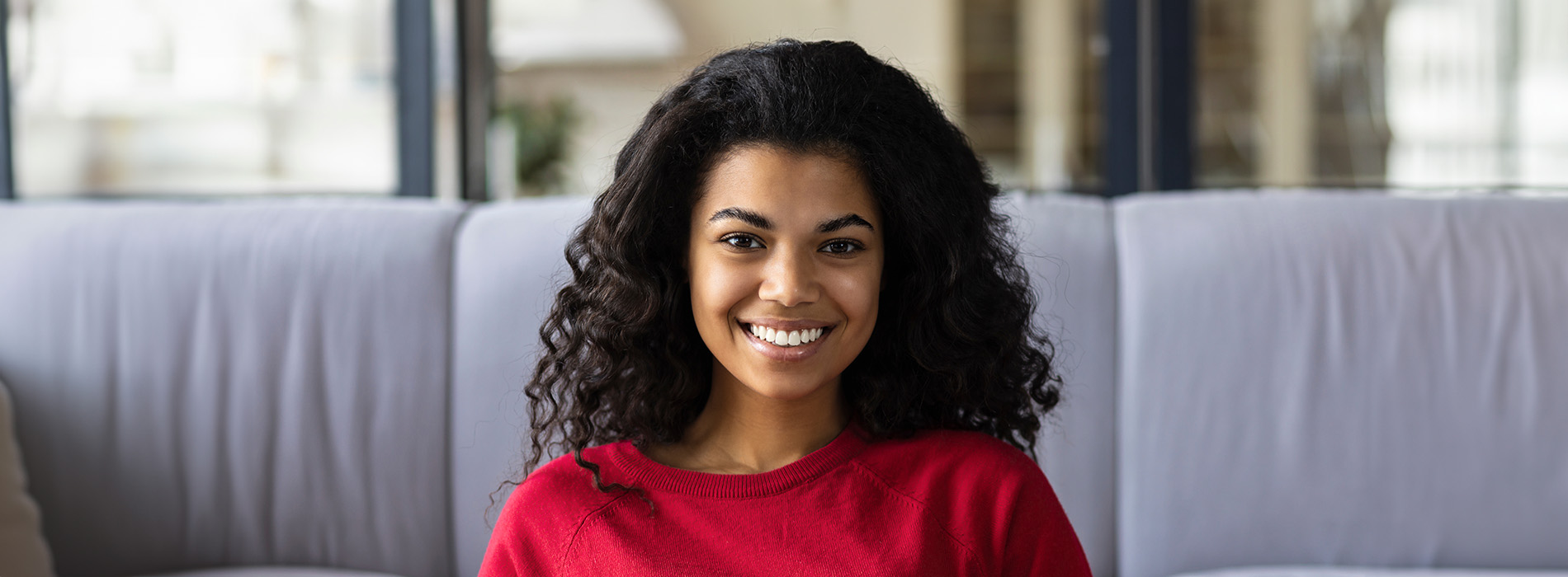 The image is a photograph of a woman with light skin, smiling at the camera. She appears to be in her late twenties or early thirties and has long hair. Her eyes are looking directly at the camera, and she is holding up her index finger near her mouth as if she s making a point or emphasizing something. The background is plain and light-colored, which suggests that this could be a stock photo used for various purposes such as advertising, personal branding, or lifestyle content.