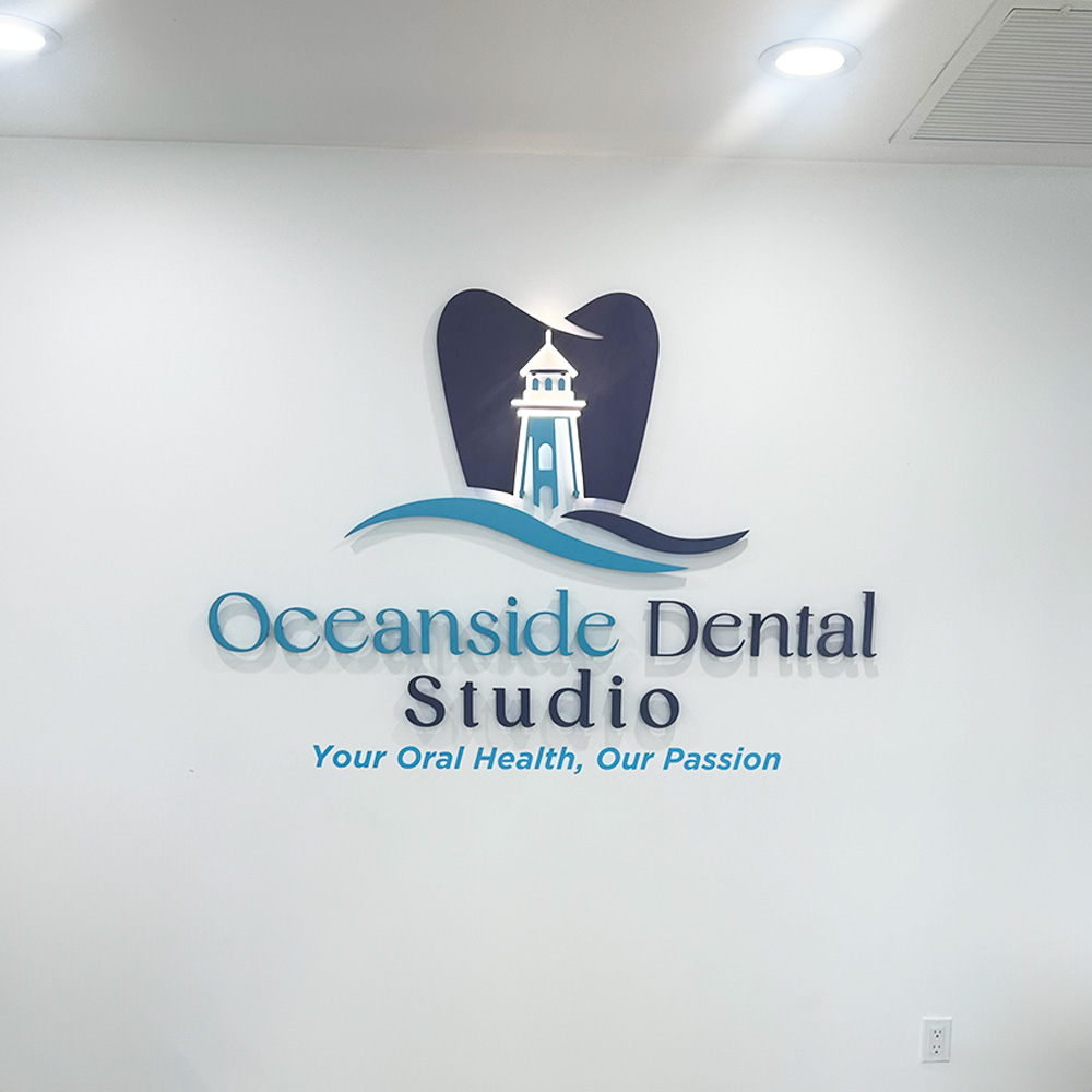The image shows an interior wall with a sign that reads  OCEANSIDE DENTAL STUDIO  prominently, accompanied by a logo featuring a stylized lighthouse and waves, against a backdrop of a clean, modern office environment.