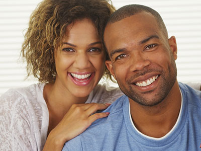 The image shows a smiling couple posing together  the man has a beard and mustache, and both are looking directly at the camera with expressions of happiness.